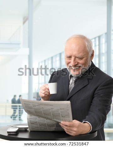 Senior businessman on coffee break in office lobby, reading papers, holding coffee cup, smiling.?