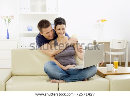 Happy young couple browsing internet on laptop computer at home, smiling.?