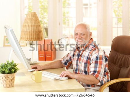 Happy senior man using computer at home, smiling at camera.?