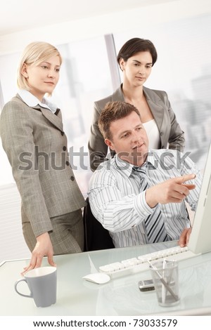 Businesspeople at work, businessman pointing at computer screen, coworkers watching.?