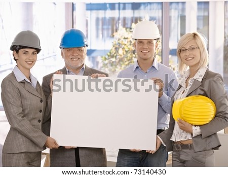 Architect team in hardhat holding blank poster for copyspace in office, smiling.?