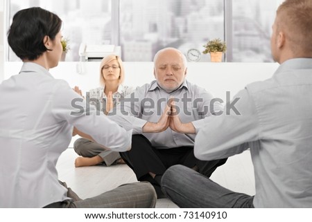 Businesspeople exercising yoga in office with eyes closed, focus on senior businessman.?