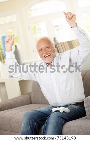 Senior man happy winning computer game, raising arms, laughing, looking at camera.?