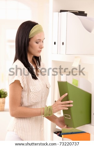 Young woman busy arranging folders on shelf.?