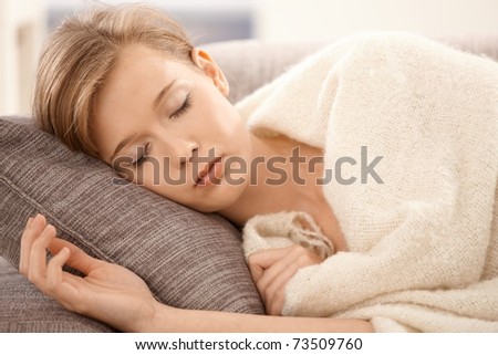 Closeup portrait of young woman sleeping on sofa at home, covered with blanket.