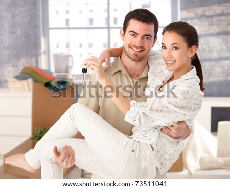 Young couple smiling happily in new house, holding keys in hand, mess around.