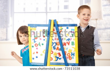 Portrait of happy kids playing together with drawing board, looking at camera, smiling.