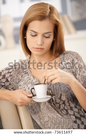 Woman having coffee on couch, holding coffee cup, stirring coffee.?