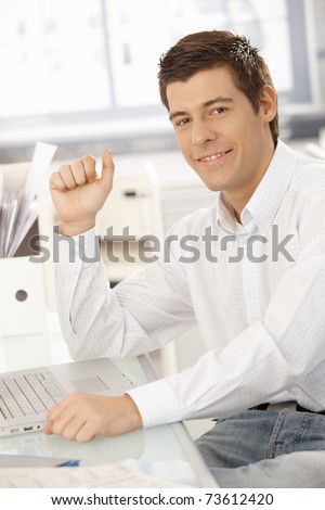 Portrait of confident young businessman sitting in office with laptop computer, smiling at camera.?