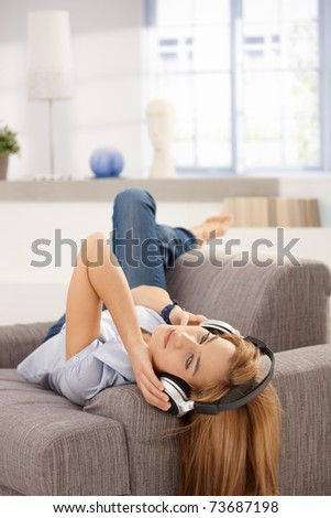 Attractive female laying on sofa, listening music through headphones.?