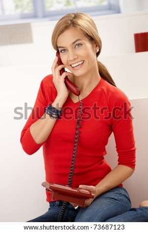 Happy woman in red pullover talking on phone sitting on floor at home.?