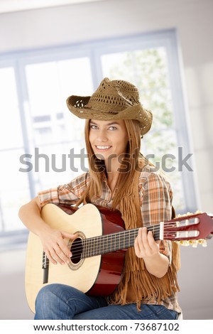 Attractive young girl playing guitar, smiling, wearing western hat.?