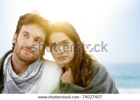 Young couple sitting on summer beach with blanket enjoying sunset.?