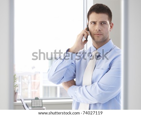 Good looking casual office worker talking on mobile phone in bright office.?