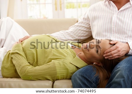 Happy pregnant woman lying on sofa in man\'s lap, man holding her head.?