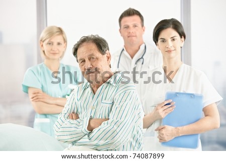 Portrait of old patient with doctors and nurse in hospital, looking at camera.?