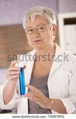 Senior teacher standing in classroom, holding test tube, teaching chemistry in elementary school.?