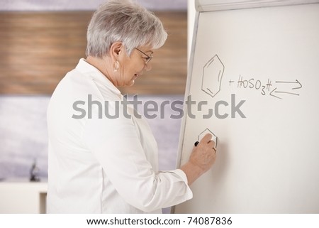 Senior teaching chemistry in school, drawing molecular formulas on whiteboard.?