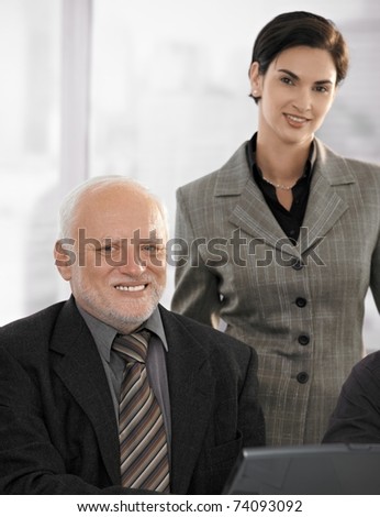 Portrait of senior businessman with mid adult female partner in office, smiling at camera.