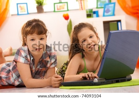 Elementary age girls playing computer game on laptop at home, looking at camera, smiling.
