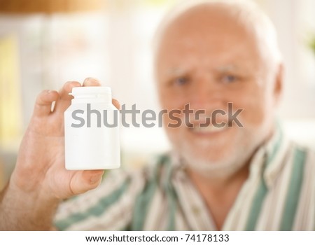 Blank medicine phial in focus handheld by elderly smiling man, copyspace.?