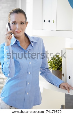 Portrait of pretty office worker on phone call, looking at camera, smiling.?