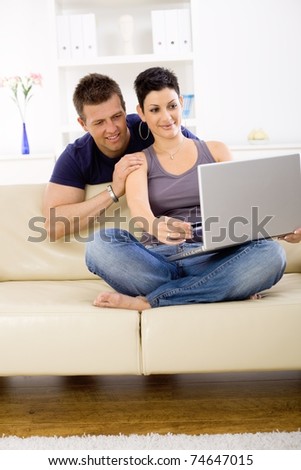 Couple using laptop computer at home together, looking at screen, smiling.?