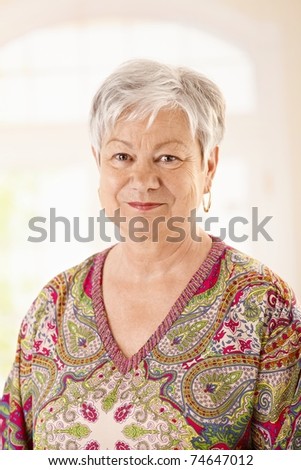 Portrait of elderly woman in colorful shirt, looking at camera, smiling.?