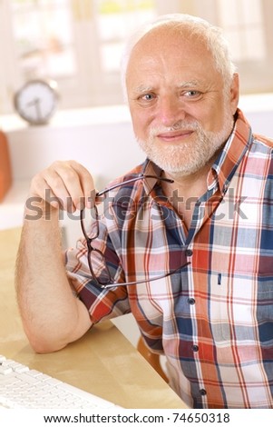 Portrait of happy older man smiling at camera, holding glasses.?