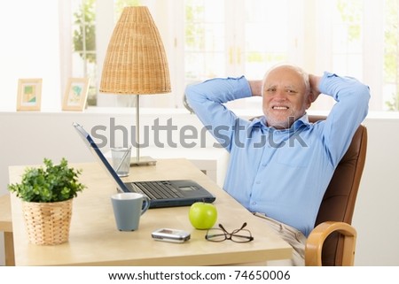 Happy elderly man smiling at desk at home, sitting relaxed with hands up on nape.?