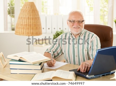 Portrait of senior professor sitting at desk, doing research work, using laptop computer, smiling at camera.?