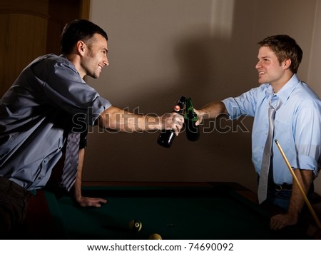Young men clinking beer bottles at snooker, smiling at each other, celebrating game.?