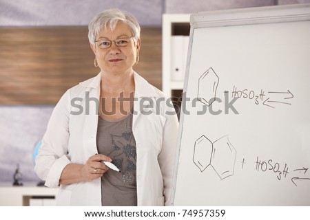Senior teaching chemistry in school, explaining molecular formulas on whiteboard.?