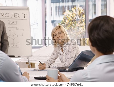 Smiling mid adult businesswoman sitting on team meeting, looking at camera.?