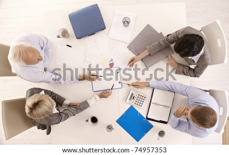 Businessteam busy working at meeting table, pointing at document, overhead view.?