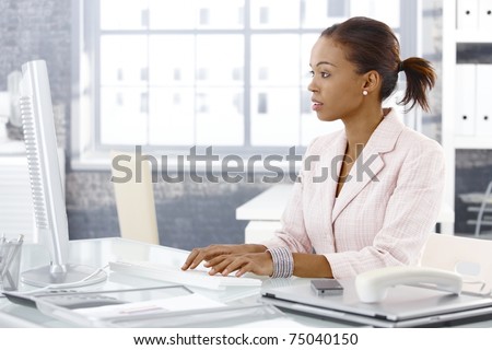 Attractive  businesswoman sitting at desk at work, using desktop computer.?