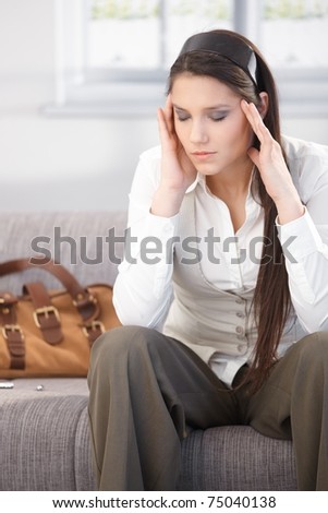 Young woman having headache after work, sitting on sofa eyes closed.?