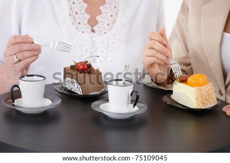 Two women sitting at coffee table, eating cake, drinking coffee, face is not visible.?