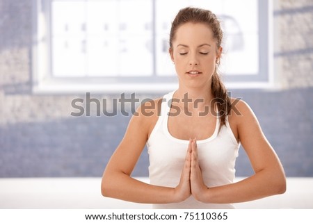 Pretty young girl practicing yoga, meditating in prayer pose in studio, eyes closed.?