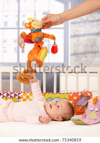 Happy baby girl playing in bed, mum holding colorful toy.?