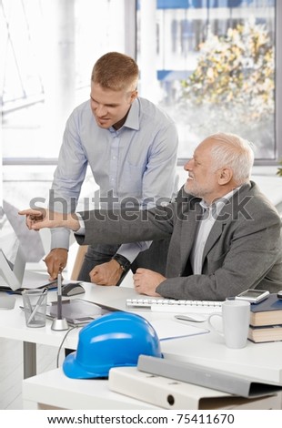 Senior and junior designers discussing work together in office, senior man pointing at screen.?