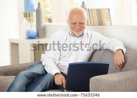 Older man sitting on sofa, smiling at computer screen at home.?