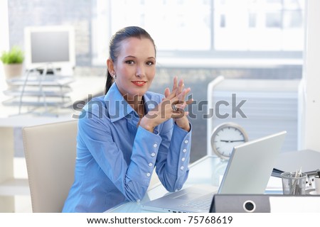 Portrait of happy office worker girl sitting at desk, smiling, looking at camera.