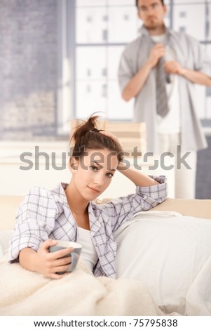 Young attractive woman drinking tea in bed in the morning, man dressing up in the background.?