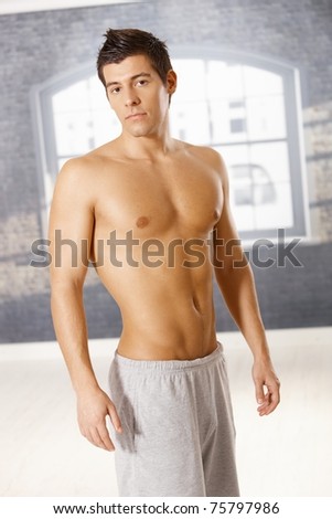 Portrait of athletic young guy posing in gym, looking at camera.?