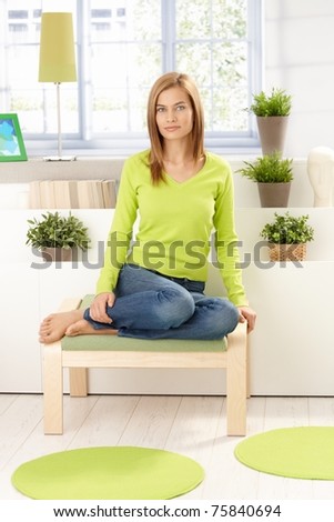 Young attractive girl sitting front of window, plants around, wearing vivid green pullover, smiling.?