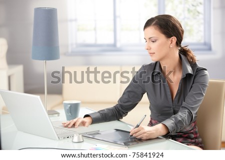 Young graphic designer working on laptop using tablet at home.?
