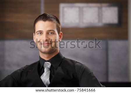Portrait of goodlooking young businessman sitting in fancy office, smiling.?