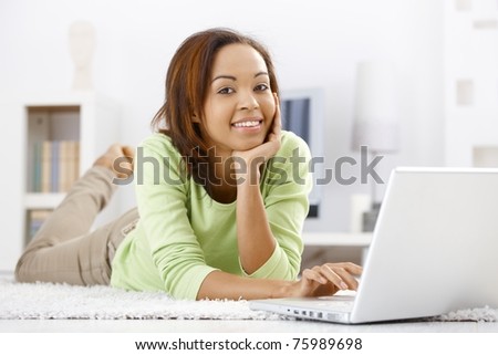 Portrait of girl lying on floor at home using laptop computer, browsing Internet, smiling at camera.?