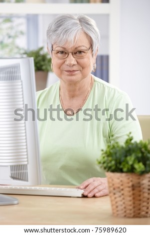 Portrait of elderly woman sitting at desk, having computer, smiling.?